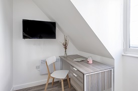 A desk and a chair facing the wall. A television is mounted on the wall to the left of the desk.